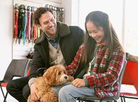 father and daughter smiling petting brown furry doodle dog