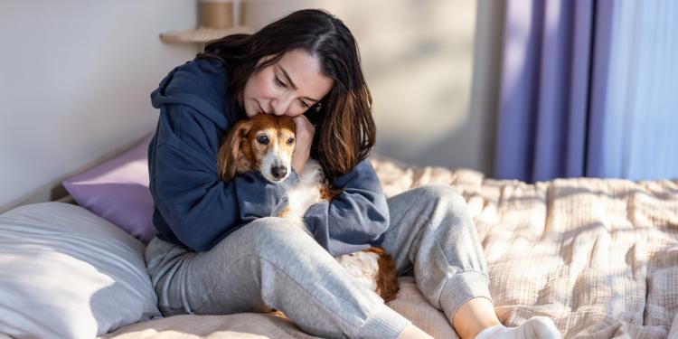 Woman hugging small dog on bed