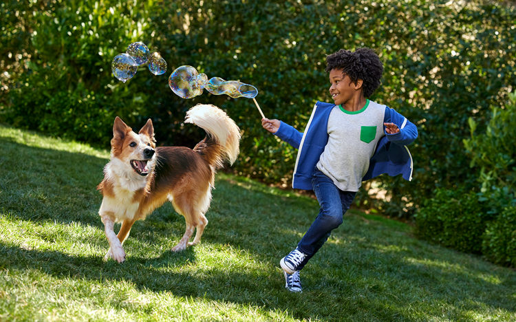 A child runs with his dog while playing with a bubble wand in a green gassy area.