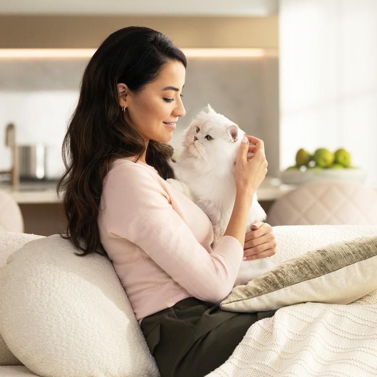 Mujer en un sofá abrazando a un gato blanco de Fancy Feast