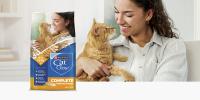 A woman smiles and looks down at an orange tabby cat; to the right sits a bag of Purina Cat Chow Complete Chicken