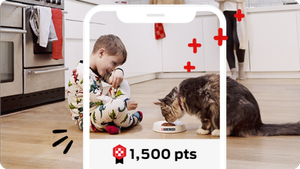 A boy sitting with his cat on the floor while the cat eats from a bowl