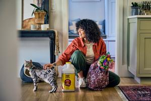 woman sits in her house petting her cat next to a jug of Purina Tidy Cats cat litter.