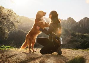 A woman kneeling down and embracing her dog.