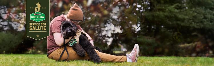 Person sitting on ground and hugging black service dog