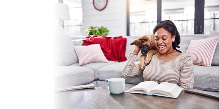 A puppy on a couch looking over its owner’s shoulder while the owner is reading on the floor