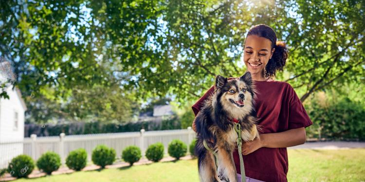 A young girl smiles as she holds her small dog.