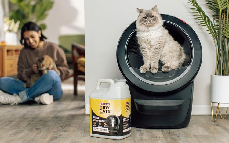 person on floor petting cat with cat in litter robot, and overlay of jug of litter